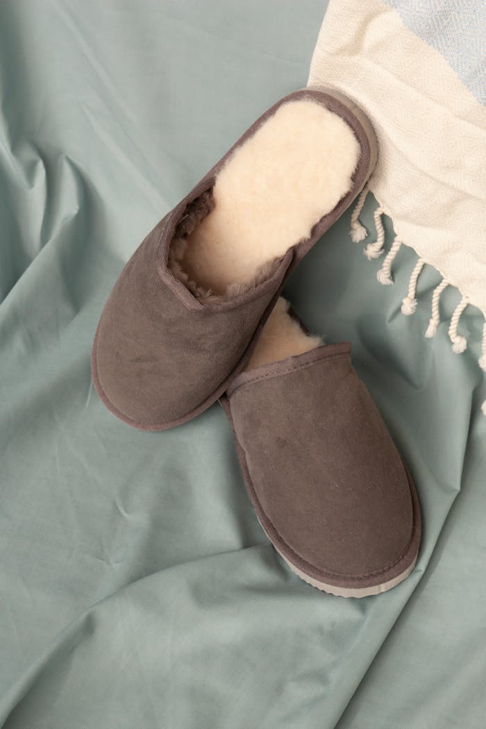 Services-01 Pair of cozy brown slippers with cream lining on soft blue fabric setting.